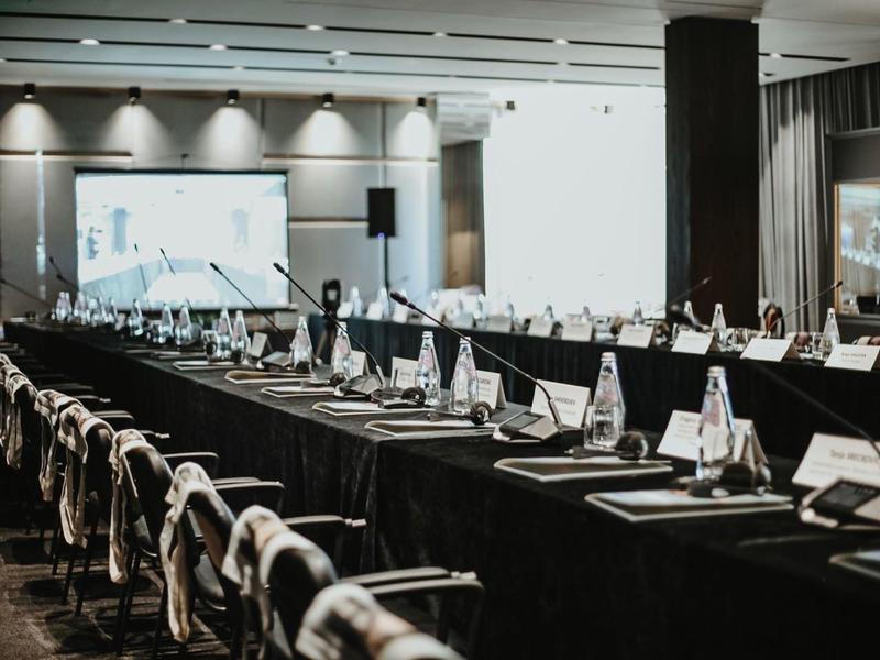 Ampia sala conferenze con lunghi tavoli, sedie e proiettore per presentazioni.