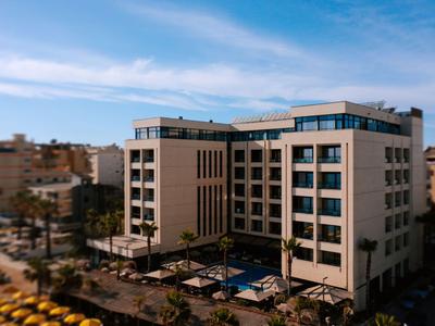 Bâtiment d'hôtel moderne avec piscine et terrasse dans une ville sous un ciel clair.