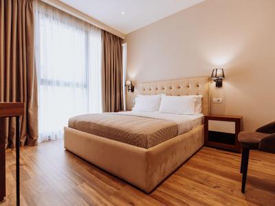 Chambre d'hôtel moderne avec grand lit, sol en bois et rideaux à la fenêtre.