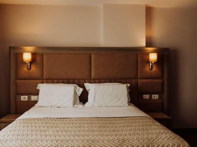 Lit double moderne avec tête de lit rembourrée et deux lampes murales dans une chambre d'hôtel.