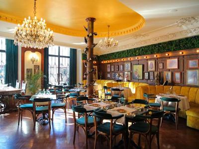 Elegant restaurant met houten lambrisering, gele banken en kroonluchters.