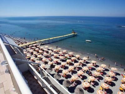 Blick von oben auf einen Strand mit Reihen von Sonnenschirmen und einem langen Steg im Meer.