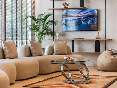 Modernes Wohnzimmer mit beige Sofa, Glas-Couchtisch, Pflanzen und Medienwand mit Fernseher.