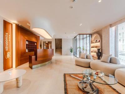 Helles Hotellobby mit geschwungenem Empfangstresen und moderner Sitzgruppe neben großen Fenstern.