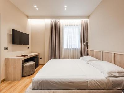 Modern eingerichtetes Schlafzimmer mit großem Bett, Fernseher und Schreibtisch nahe Fenster mit Vorhängen.