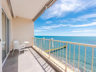 Balkon mit Aussicht auf das blaue Meer, zwei Stühle und ein kleiner Tisch bei klarem Himmel.