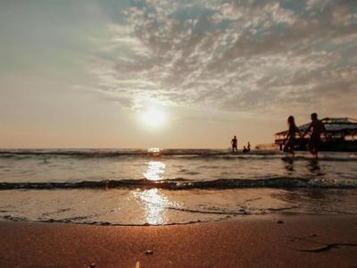 Sunset at the beach with people in the water and on the shore.