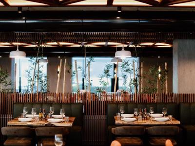 Modern restaurant interior with wooden furniture and green plants behind a partition.