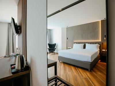 Modern hotel room with large bed, wooden floor, and armchair by the window.