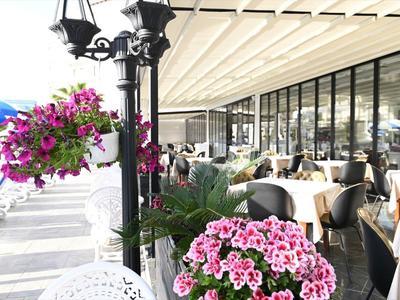 Zona exterior de restaurante con mesas preparadas y arreglos florales bajo una terraza con toldo.