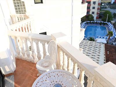 Balcón con mesa redonda y silla, vista a piscina y edificio adyacente.