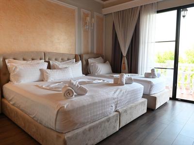 Habitación de hotel luminosa con cama grande, banco y balcón con vista al verde.