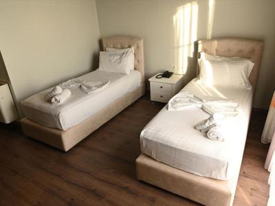 Dos camas individuales con ropa blanca y toallas en una habitación de hotel luminosa con suelo de madera.