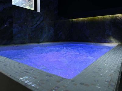 Vista de un jacuzzi moderno con agua iluminada en azul en una habitación oscura.