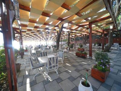 Überdachte Terrasse mit Tischen und Stühlen, umgeben von Pflanzen und natürlichem Licht.