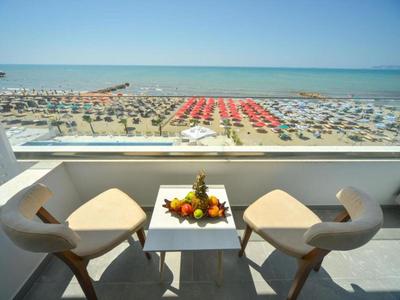 Balkon mit Tisch und zwei Stühlen mit Meerblick und Strand mit Sonnenschirmen im Hintergrund.