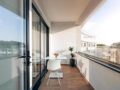 Moderní balkon s dřevěnou podlahou, bílou židlí, stolem a rostlinou v hotelu.
