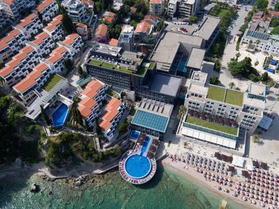 Vista aérea de un complejo hotelero en la playa con piscina circular y tumbonas junto al agua
