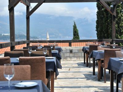 Terrasse eines Restaurants mit blau gedeckten Tischen und Blick auf Berglandschaft und Wasser
