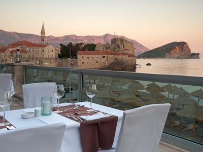 Elegantes Restaurant mit gedeckten Tischen auf einer Terrasse mit Blick auf das Meer und historische Gebäude.