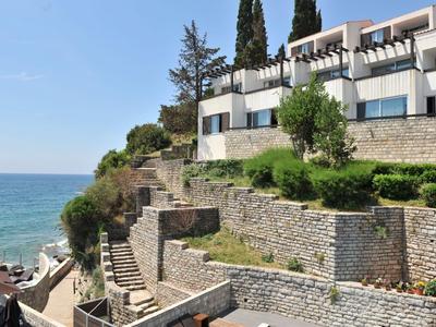 Mehrstöckiges Hotel mit Terrasse am Hang über dem Meer bei sonnigem Wetter.