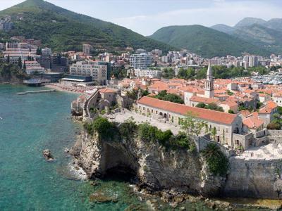 Vista de una ciudad costera con edificios históricos en un acantilado y montañas al fondo.