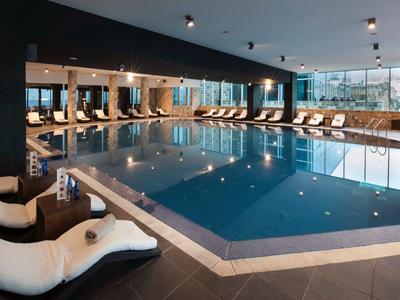 Piscina cubierta con tumbonas y grandes ventanas, ambiente moderno y elegante.