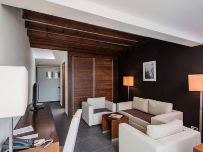 Habitación de hotel con mobiliario moderno, área de estar, paredes de madera y luz cálida.
