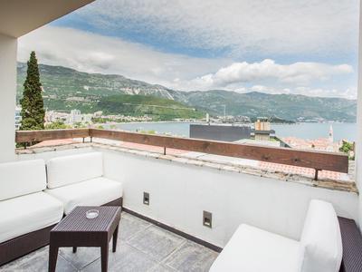 Terraza con sillones blancos y mesa pequeña con vista a montañas y un lago bajo cielo nublado.