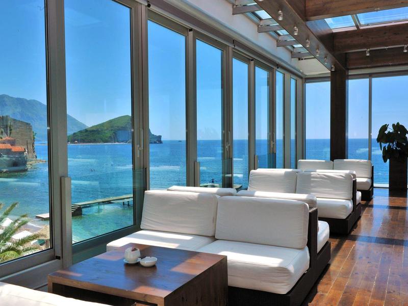 Hotel moderno con sofás blancos frente a grandes ventanas y vista al mar en día soleado.