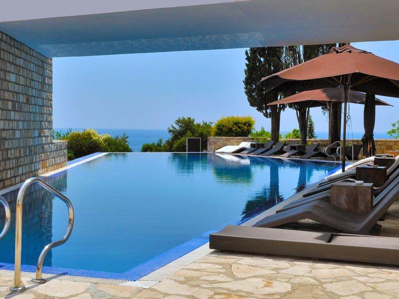 Piscina infinita con vista al mar, rodeada de muros de piedra y tumbonas bajo un pabellón.