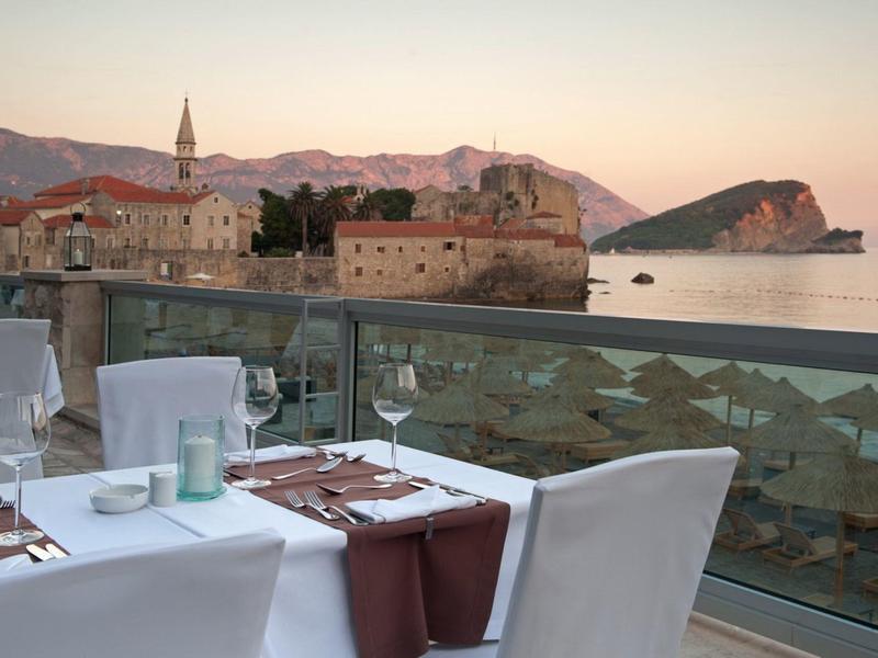 Elegante restaurante al aire libre con vista a un casco antiguo y el mar al atardecer.