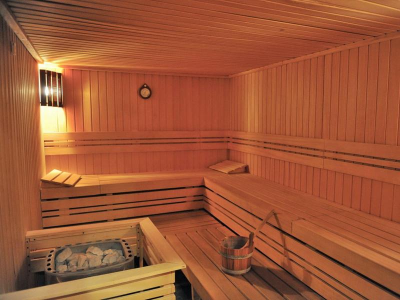 Sala de sauna con revestimiento de madera, bancos para sentarse y cubeta de sauna con cucharón.