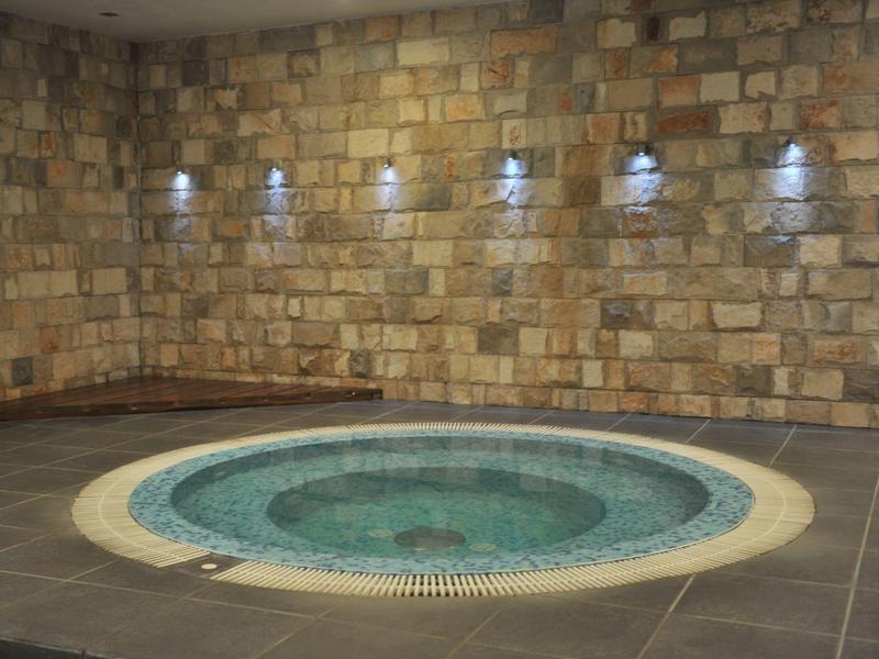 Jacuzzi redondo con asientos en una habitación con paredes de piedra y suelo gris.