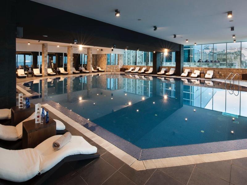 Piscina cubierta con tumbonas y grandes ventanas, ambiente moderno y elegante.