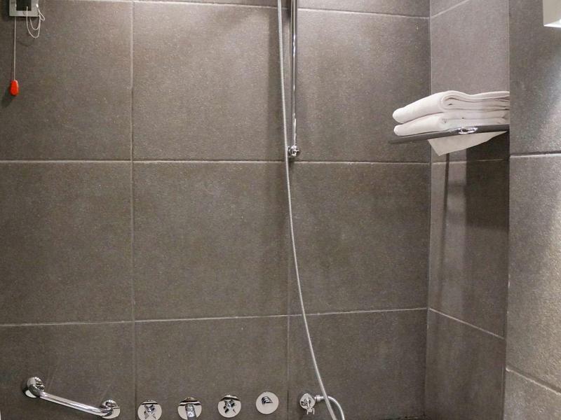 Baño moderno con bañera blanca, ducha de mano y toallas blancas en una repisa.