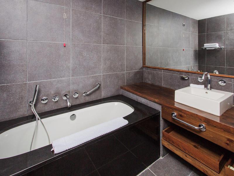 Baño moderno con tocador de madera marrón, lavabo blanco y bañera grande.