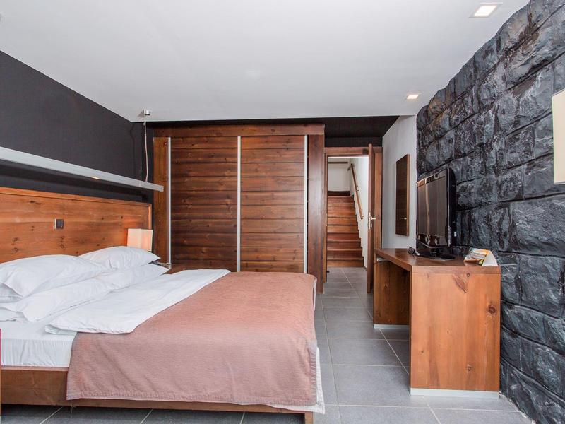 Habitación de hotel moderna con cama doble, muebles de madera y pared de piedra en tonos neutros.