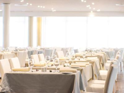 Restaurante moderno y luminoso con mesas preparadas y sillas blancas, mucha luz natural.