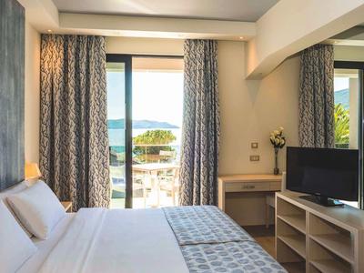 Hell eingerichtetes Schlafzimmer mit großem Fenster, Bett in Weiß und Fernseher auf Regal.