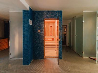 Área moderna de bienestar con sauna, duchas de vidrio y azulejos azules en la pared.