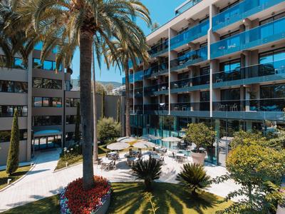 Hotelaußenbereich mit Pool, Liegestühlen, Palmen und mehreren Etagen mit Balkonen.