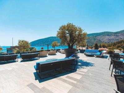 Terraza exterior moderna con sofás azules, mesas y vista a colinas bajo un cielo despejado.