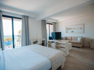 Habitación de hotel moderna con vista al mar, cama doble y área de estar acogedora con televisor.