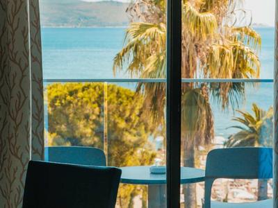 Vista desde una habitación con balcón de palmeras y el mar en un día soleado.