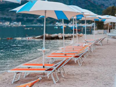 Varias tumbonas naranjas con sombrillas azules y blancas en la playa junto a agua tranquila.