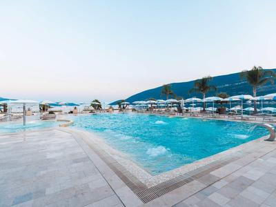 Moderner Hotelpool mit Liegestühlen und Sonnenschirmen, Blick auf Hügel und Meer.