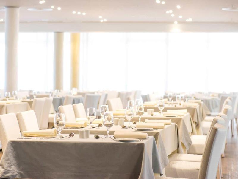 Restaurante moderno y luminoso con mesas preparadas y sillas blancas, mucha luz natural.