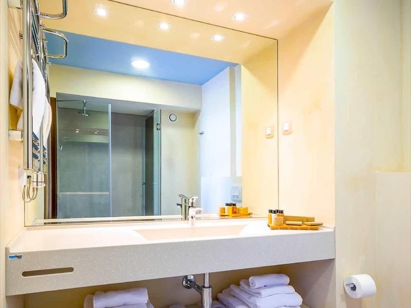 Baño moderno con gran espejo y estantes debajo con toallas blancas.