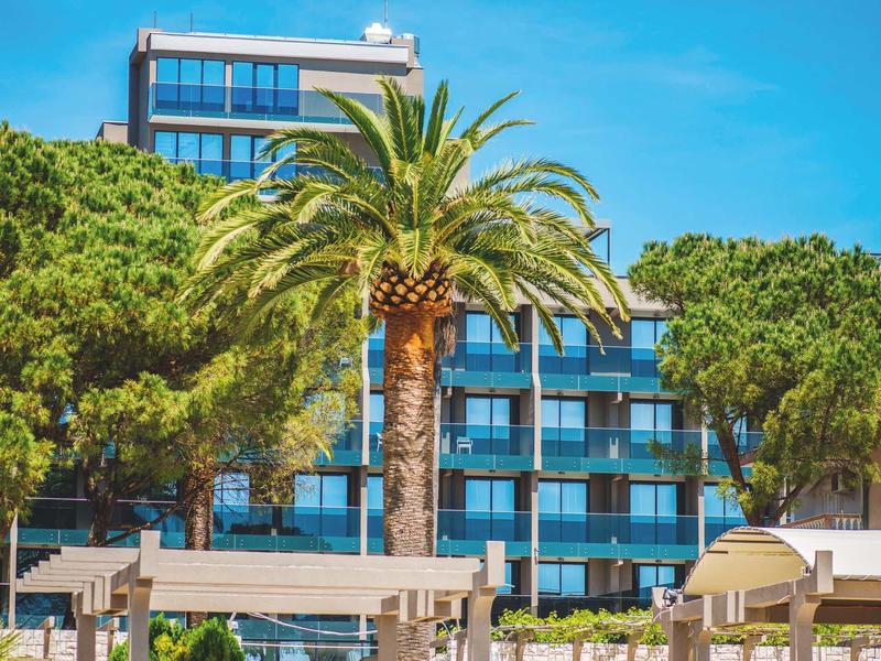 Edificio de hotel moderno con grandes ventanas y palmeras en primer plano bajo cielo azul.
